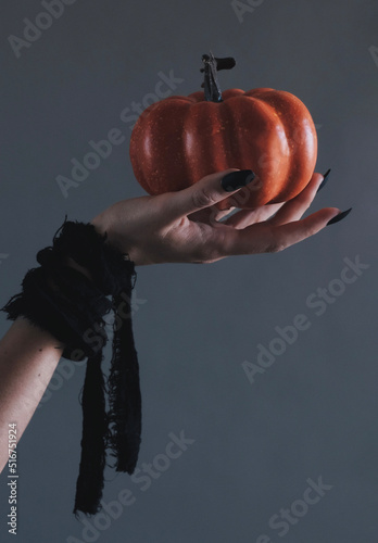 Close up halloween pumpkin in the witch's hand with long black nails. Halloween aesthetic. Black witch.
