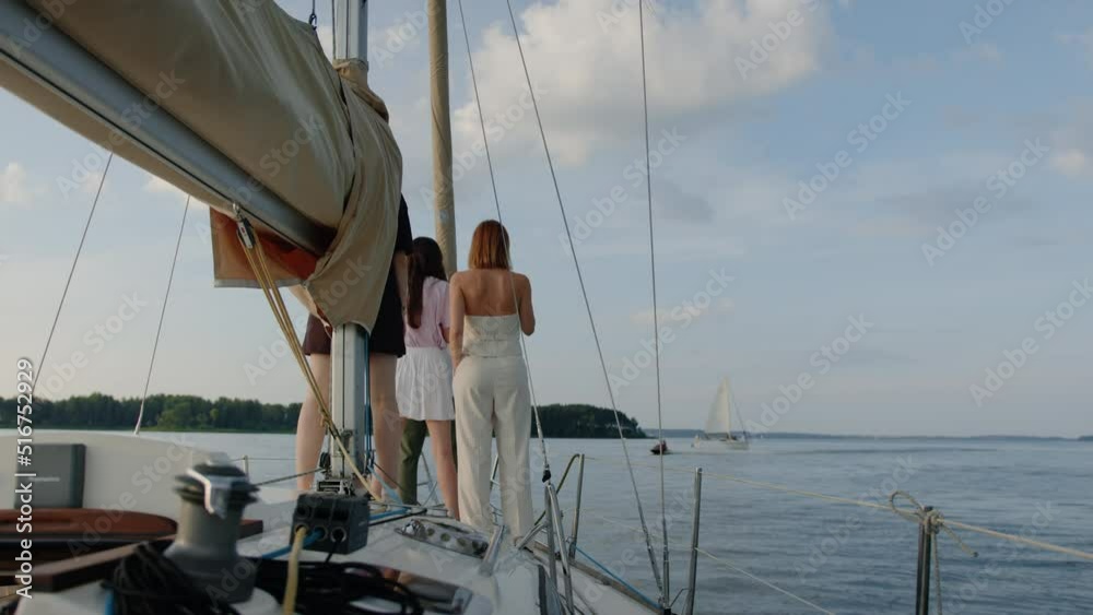 Friends are standing on the bow of a sailing boat and drinking wine Friends are standing on the bow of a sailing boat and drinking wine