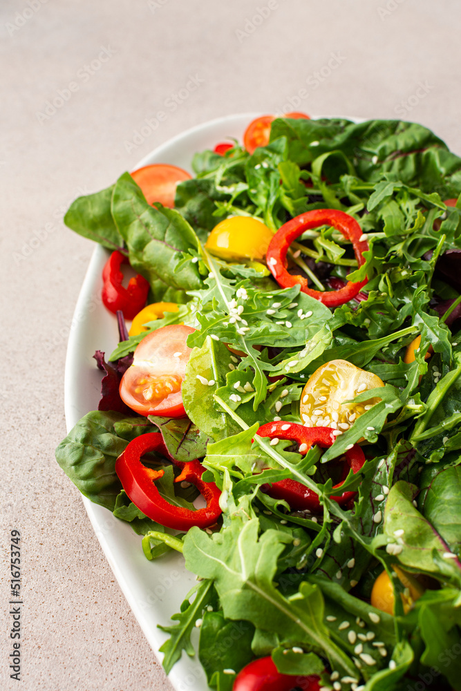 Salad of fresh farm vegetables in an oval dish on a pink background, sitya lettuce and chard, tomatoes and colorful bell peppers, arugula and sesame seeds Salad of fresh farm vegetables in an oval dish on a pink background, sitya lettuce and chard, tomatoes and colorful bell peppers, arugula and sesame seeds
