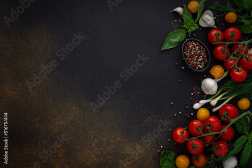 Food background, fresh ripe red and yellow tomatoes, spices and basil leaves, garlic and green onions on a dark background, healthy food concept, copy space, top view