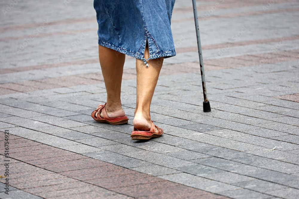Foto de Old woman walking with cane on summer street, legs on sidewalk