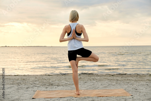 fitness, sport, and healthy lifestyle concept - woman doing yoga tree pose on beach over sunset