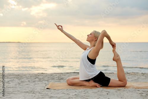 fitness  sport  and healthy lifestyle concept - woman doing yoga pigeon pose on beach over sunset