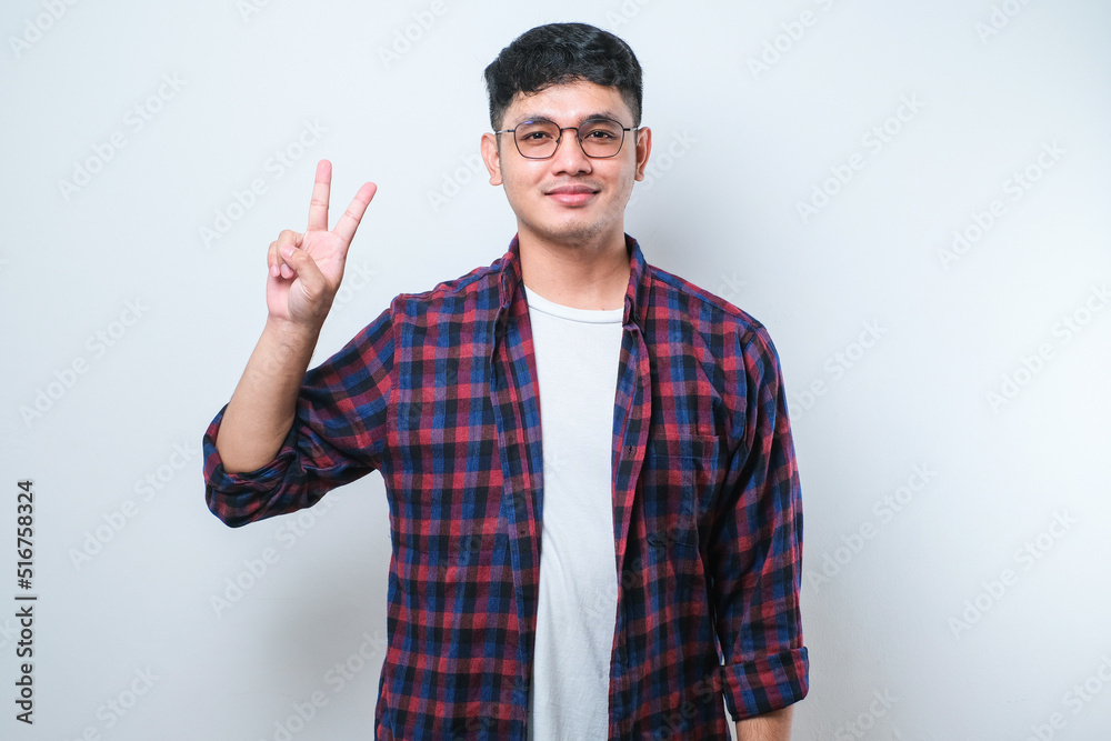 Young handsome Asian man wearing casual clothes showing and pointing up with fingers number two while smiling confident and happy Young handsome Asian man wearing casual clothes showing and pointing up with fingers number two while smiling confident and happy