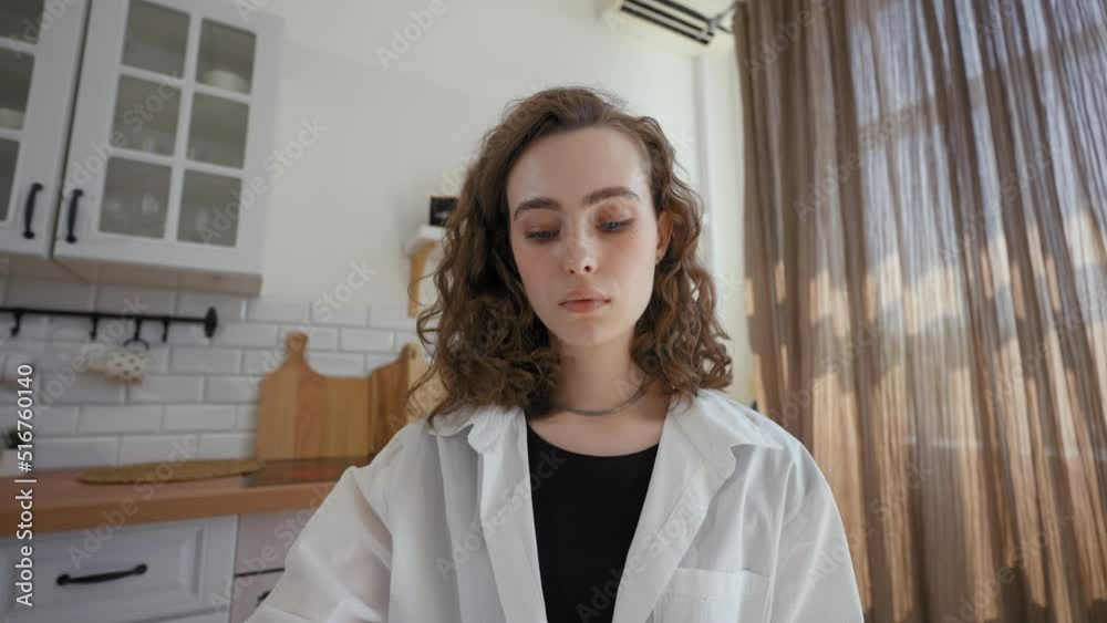 POV of young woman watching online courses on laptop making notes with pen. Female student sits at table in kitchen against window close view