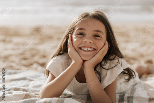 Tableau sur toile Delighted stylish kid with hands on cheeks relaxing on sandy seashore