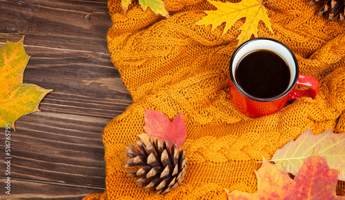 Orange knitted blanket, mug of tea, autumn leaves on a wooden background.