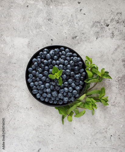 Plate with fresh blueberries and sprig of mint on a light background.