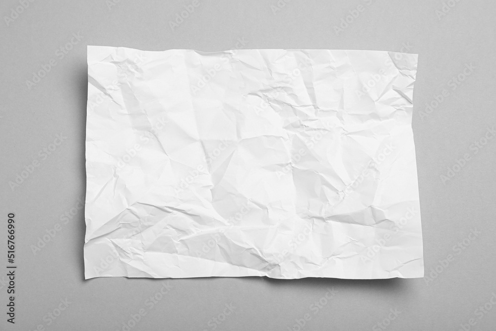 Sheet of white crumpled paper on grey background, top view