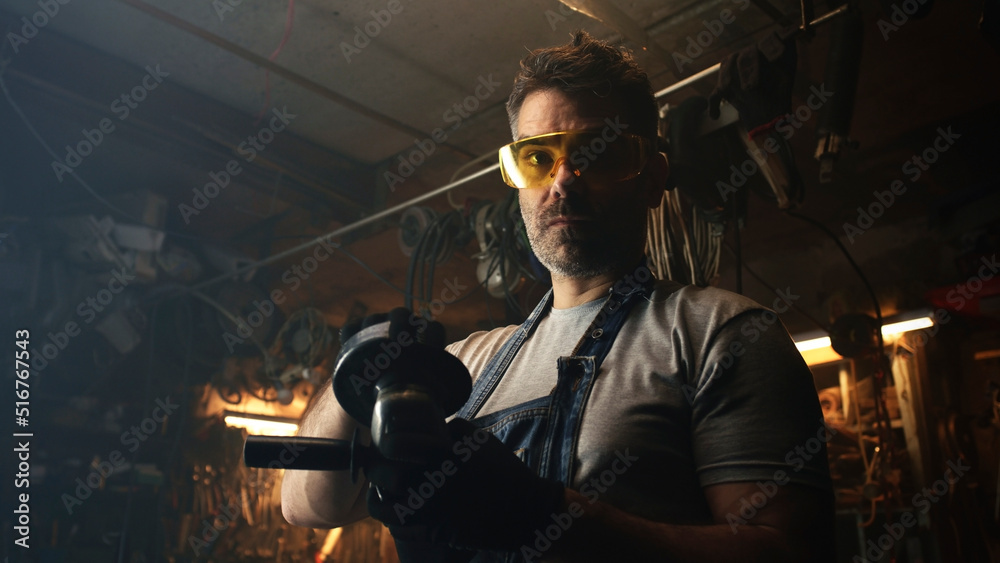 Middle aged professional worker in protective uniform and goggles preparing equipment to processing metal for his products in modern garage