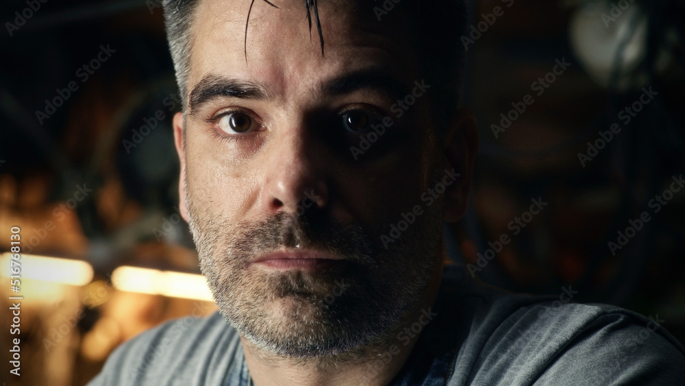 A middle-aged man looking at camera, while doing hard metal grinding work in a garage for his small business.