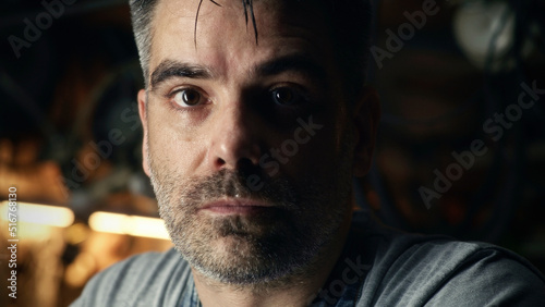 A middle-aged man looking at camera  while doing hard metal grinding work in a garage for his small business.