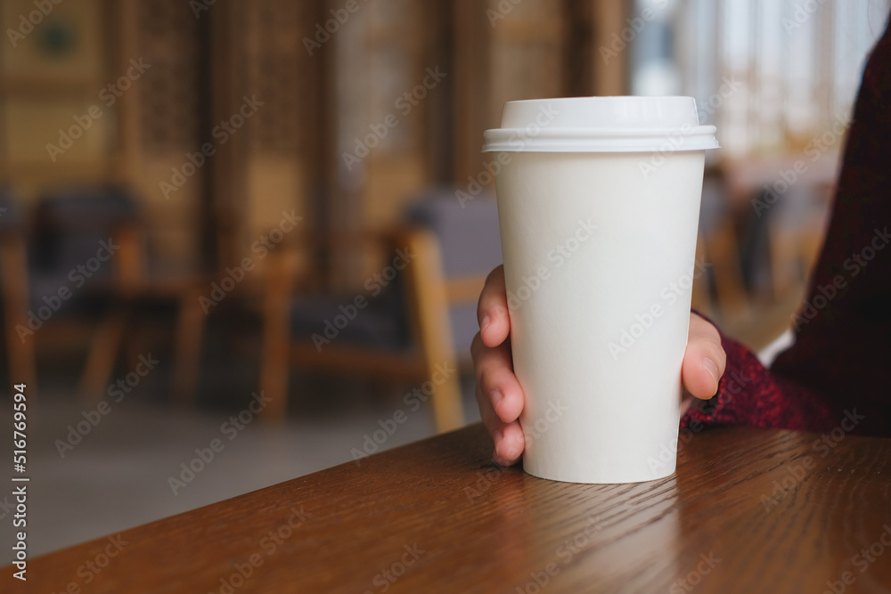 Woman hand holding coffee paper cup on wooden table in coffee cafe.