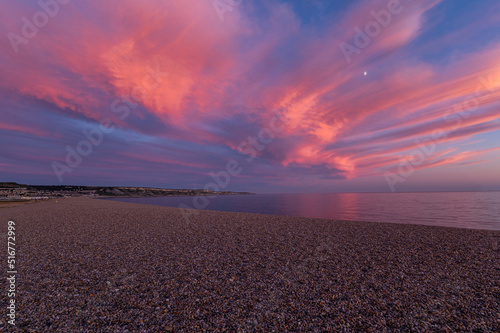 Pink sky as the sun set at Chesil beach with bank of shingle and flat calm sea reflecting the pink glowing clouds along the Jurassic coast of Dorset. photo