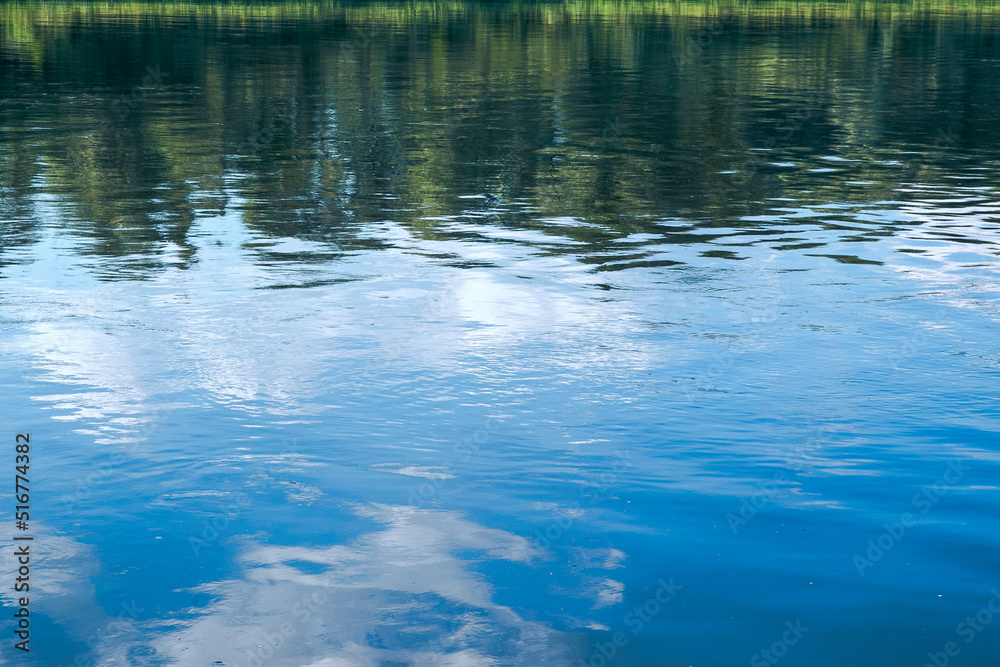 The rhythm of the waves on the river. Reflection of blue sky and green forest. 
Reflection in the river on a summer sunny day.