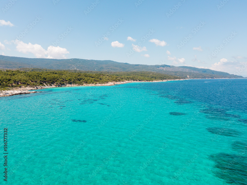 Aerial view of scenic and clear turquoise sea water from above  with white rocks and green trees around,  Mediterranean travel concept, Portokali beach in Sithonia, Greece 