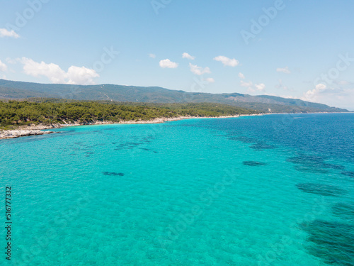 Aerial view of scenic and clear turquoise sea water from above with white rocks and green trees around, Mediterranean travel concept, Portokali beach in Sithonia, Greece 