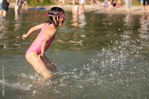 Fototapeta Naklejka Na Ścianę i Meble -  Little girl having fun in lake splashing water on summer sunny hot day outdoors