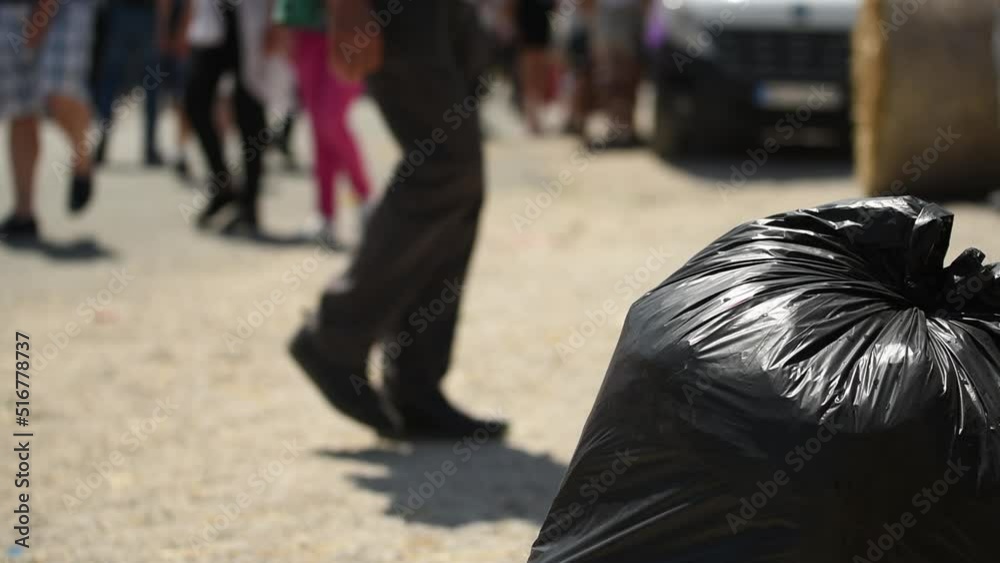 Littering and pollution in city, black garbage bag on the street with people pedestrians walking by