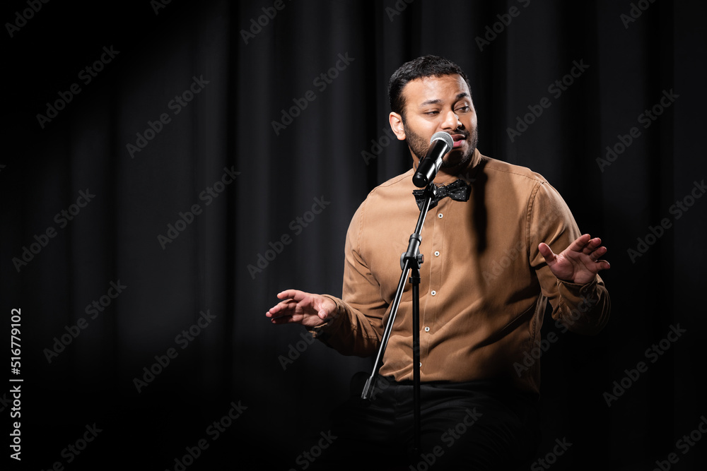 indian comedian gesturing and performing stand up comedy while telling jokes in microphone on black. indian comedian gesturing and performing stand up comedy while telling jokes in microphone on black.