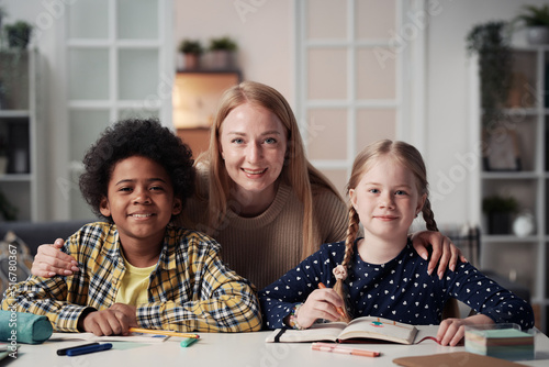Portrait of happy foster mother smiling at camera together with her adopted children at table at home photo