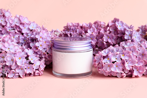 Mockup white jar with metal screw cap of moisturizing cream and lilac flowers on pink background. Closeup  summer skin care cosmetic. Product branding  cream lotion  moisturizer. Front view.