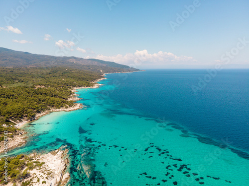 Aerial view of scenic and clear turquoise sea water from above with white rocks and green trees around, Mediterranean travel concept, Portokali beach in Sithonia, Greece 