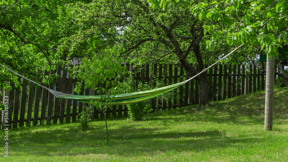 Summer garden with hanging hammock for relaxation. Hammock in backyard on the fence background.