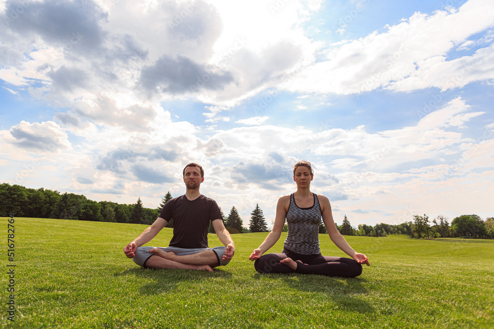 Young couple meditating in lotus position while doing yoga in park
