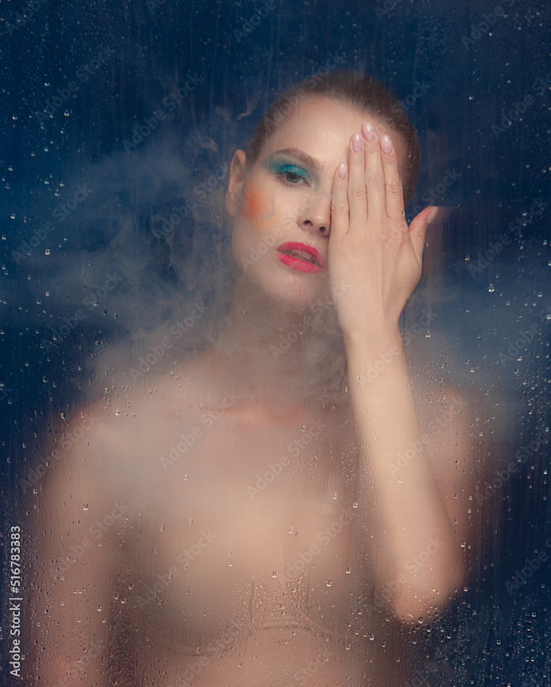 Portrait of beautiful woman with bright makeup posing in underwear isolated over dark blue background. Foggy glass effect. Pink lipstick