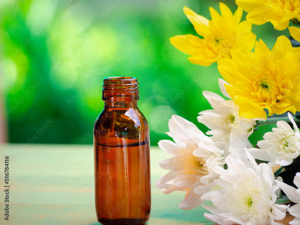 The essential oils extract and medical flowers herbs near the white and yellow flower on wooden table. The essential oil organic bio alternative medicine, brown bottle.
