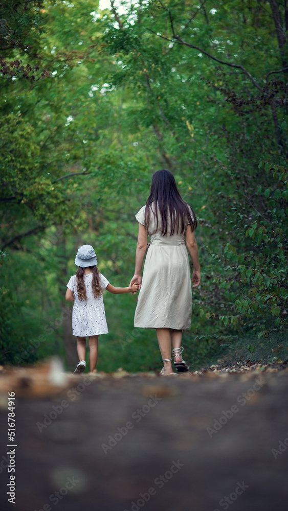 A young woman and her cute dughter holding hands are walking in the park enjoying a beautiful day A young woman and her cute dughter holding hands are walking in the park enjoying a beautiful day