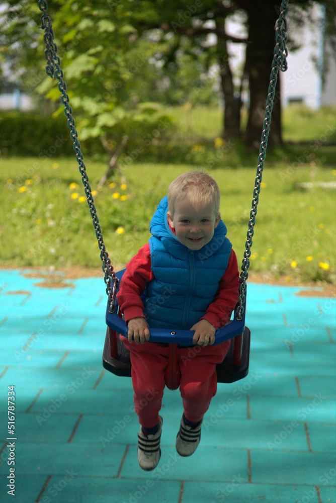 A 2-year-old blond-haired boy plays outside and swings on a swing