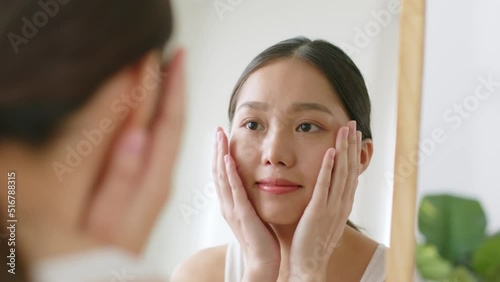 Young Asian woman touching healthy facial skin look at mirror