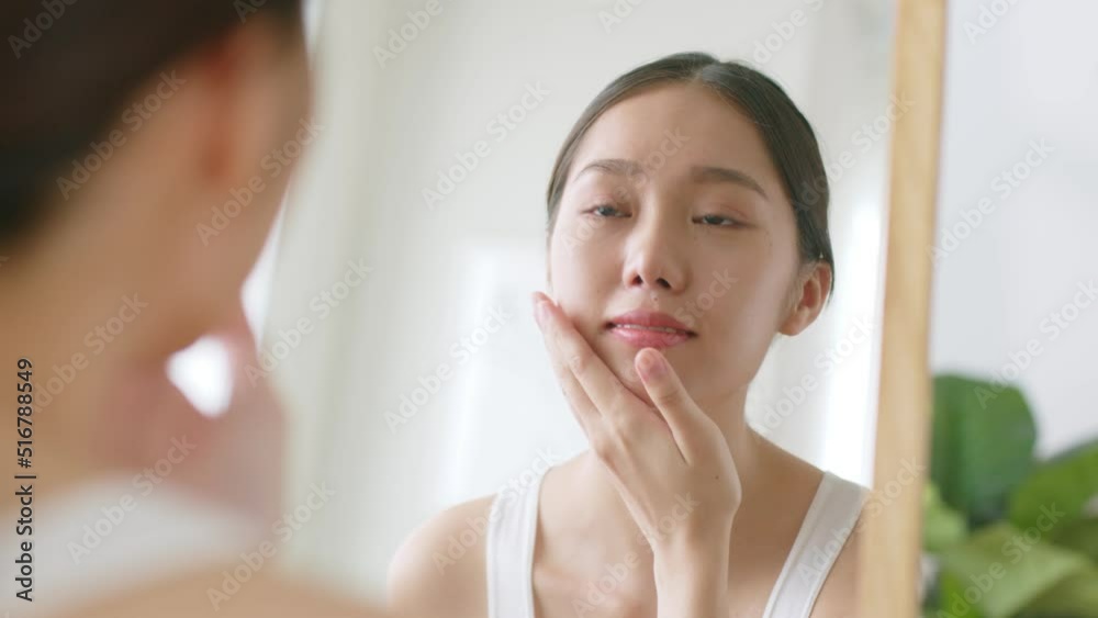 Young Asian woman apply finishing spray on face and look at mirror Young Asian woman apply finishing spray on face and look at mirror