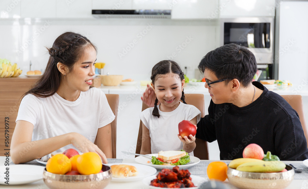 A happy Asian family spends lunch, vegetables, fruit, and dates at the table in their home. Cute little daughter having fun talking. Father, mother