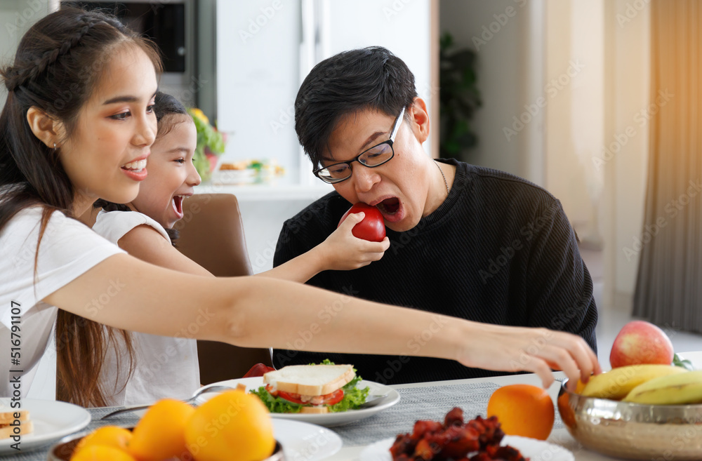 A happy Asian family spends lunch, vegetables, fruit, and dates at the table in their home. Cute little daughter having fun talking. Father, mother A happy Asian family spends lunch, vegetables, fruit, and dates at the table in their home. Cute little daughter having fun talking. Father, mother