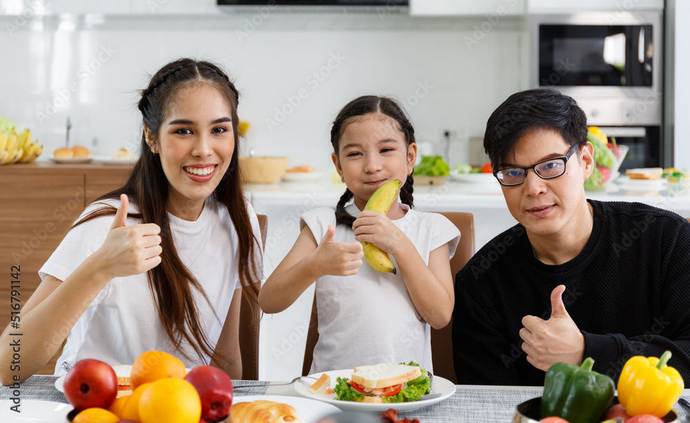 A happy Asian family spends lunch, vegetables, fruit, and dates at the table in their home. Cute little daughter having fun talking. Father, mother