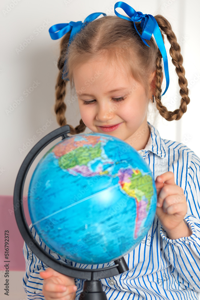 Pretty little European girl kid 6-7 years old holds a world globe in her hand. Distance online learning at home in quarantine. Back to school, learning lessons. Pretty little European girl kid 6-7 years old holds a world globe in her hand. Distance online learning at home in quarantine. Back to school, learning lessons.