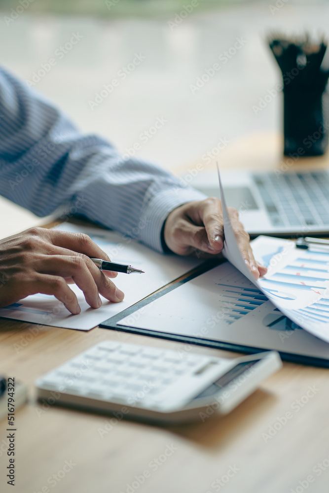 Businessman hand holding a pen to work with charts, graphs and analyze business strategies. financial statistics with laptop sit at desk vertical view Businessman hand holding a pen to work with charts, graphs and analyze business strategies. financial statistics with laptop sit at desk vertical view