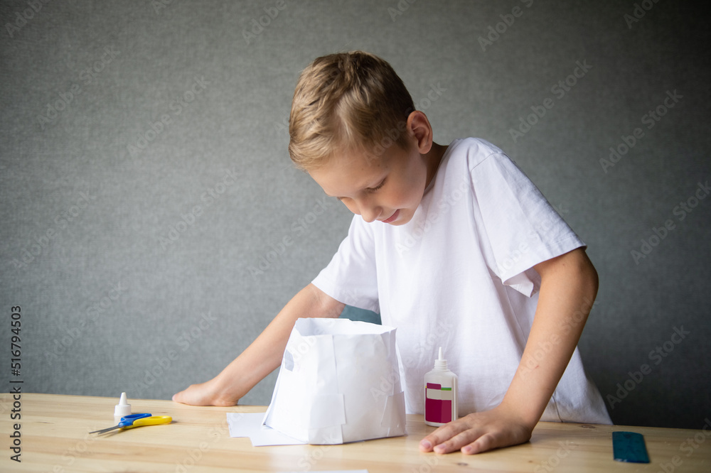 The boy cuts out details from paper. Glue the parts together with glue The boy cuts out details from paper. Glue the parts together with glue