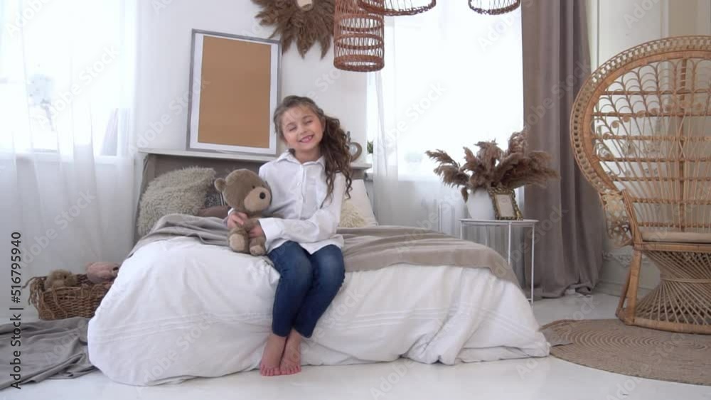Slow Motion Little cute beautiful girl sits on a bed with a soft teddy bear toy Slow Motion Little cute beautiful girl sits on a bed with a soft teddy bear toy