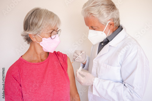 Doctor giving injection to senior caucasian woman, female receiving booster of covid 19 vaccine, people wearing mask © luciano