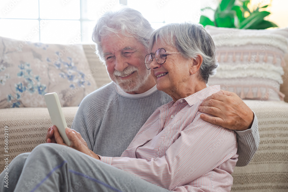 Smiling beautiful caucasian senior couple sitting on the floor at home using smart phone, old people and new technologies concept Smiling beautiful caucasian senior couple sitting on the floor at home using smart phone, old people and new technologies concept