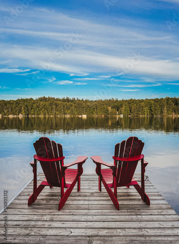 Fotografie Two red adirondack chairs on the end of a dock overlooking a lake