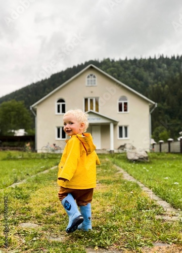 A toddler in a yellow raincoat near the house. photo