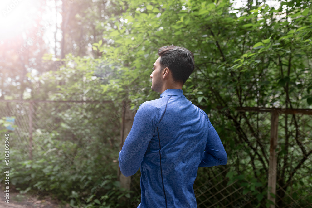 Side view on handsome man in blue sportswear jogging in the wood at the morning time Side view on handsome man in blue sportswear jogging in the wood at the morning time