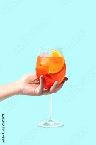 Aperol Spritz cocktail on a girls hand on blue background