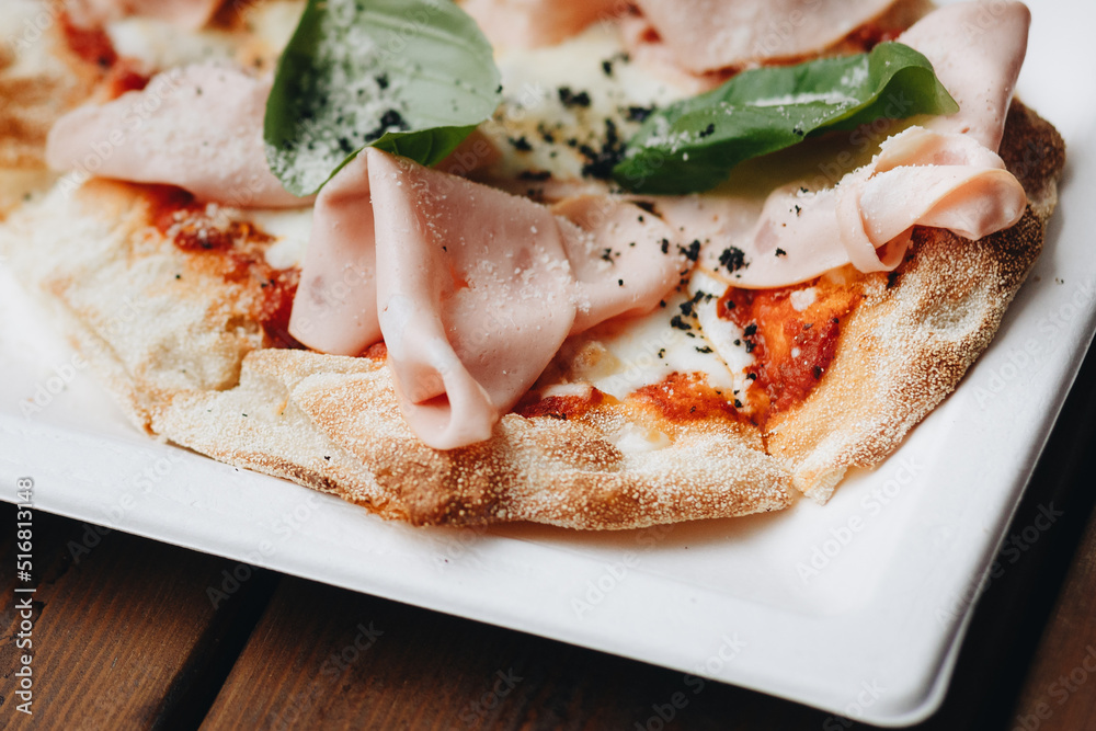 Fresh baked pizza with melted cheese, Italian herbs and tomato sauce and fresh basil on a white plate on a kitchen background, selective focus Fresh baked pizza with melted cheese, Italian herbs and tomato sauce and fresh basil on a white plate on a kitchen background, selective focus