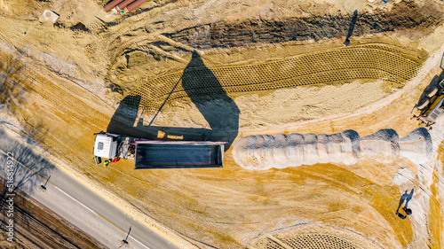 Aerial view on tipper truck is unloading gravel from trailer over construction site for new traffic roundabout photo